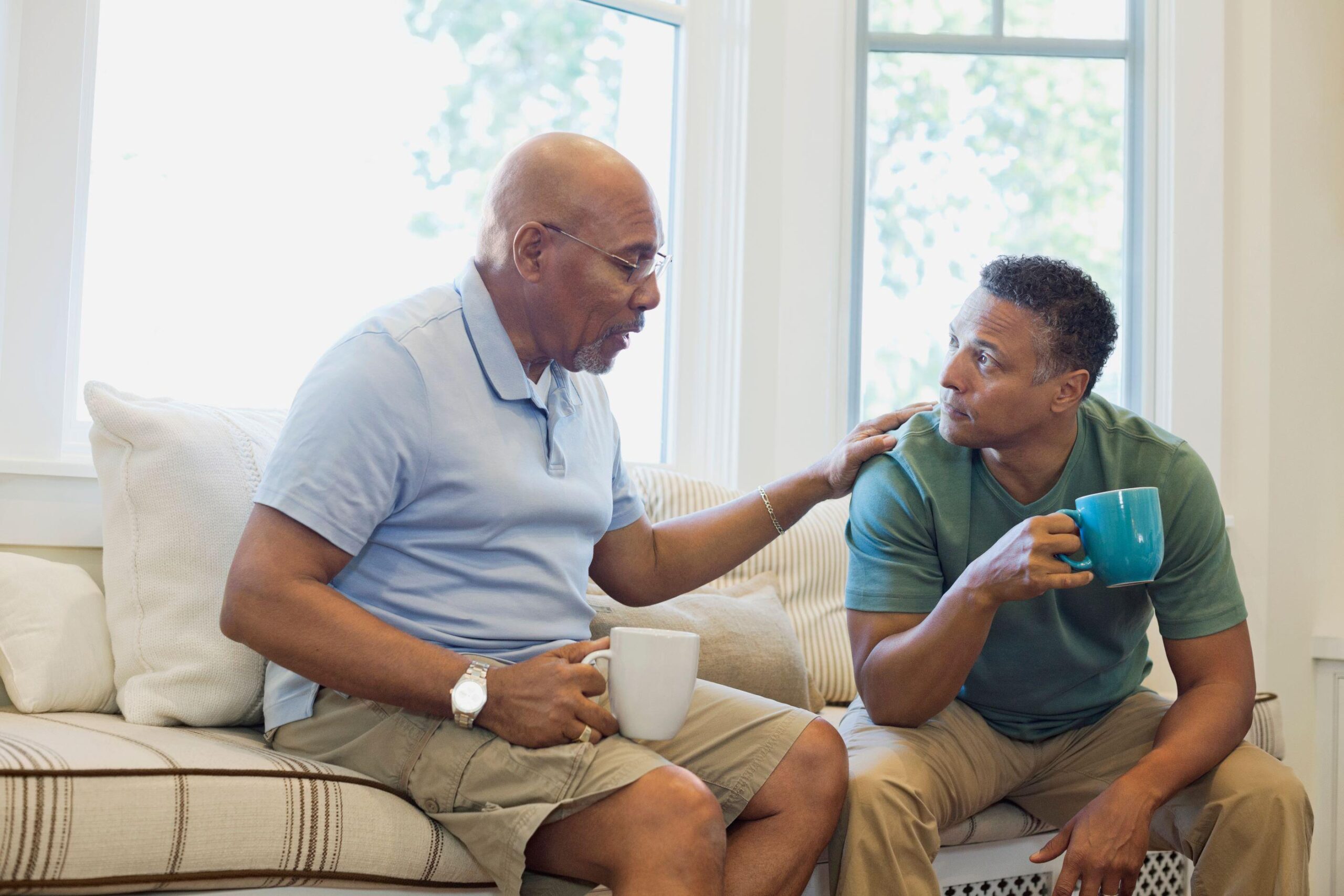 Senior-father-and-son-talking-while-having-coffee-on-sofa-AdobeStock_434384834_resized